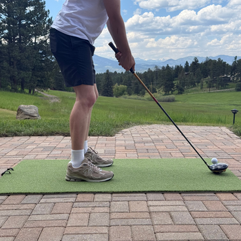 A man practicing golf in his backyard. Standing on a turf hitting mat with a driver