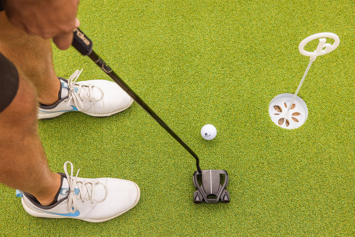 person gripping a putter ready to putt near golf hole