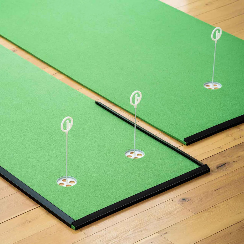 Two BirdieBall Indoor Putting Green - Classic Depth Putting Mats with white flags on a light wood floor create a realistic indoor golf practice area.