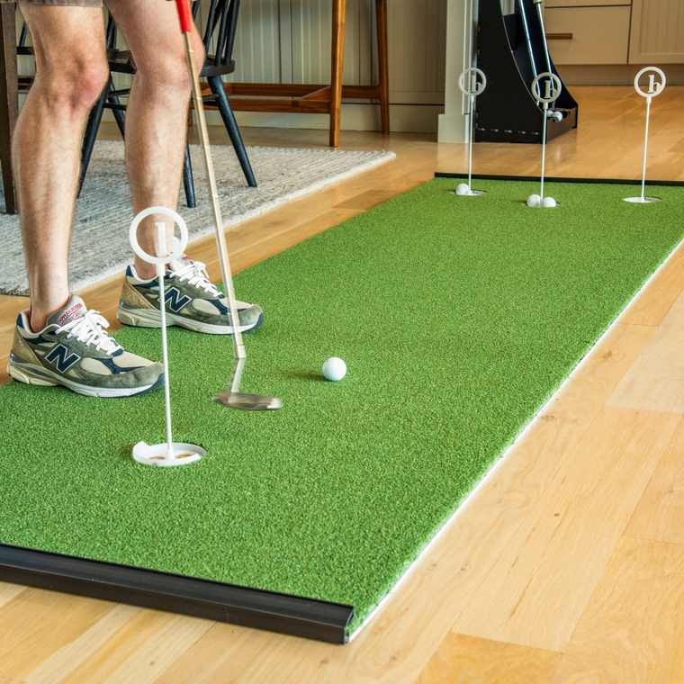 Wearing sneakers and shorts, a person practices putting with golf targets and white balls on the BirdieBall Outdoor Putting Green—Backyard Tour Grade Synthetic Turf, showcasing their skills on this realistic practice surface.