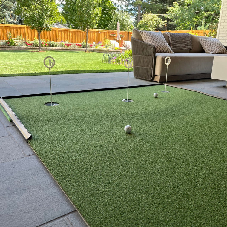 BirdieBall's Full Width Hole Deepening/Break Shim, designed for use with turf mats, is shown on a patio near outdoor furniture and a grassy backyard.
