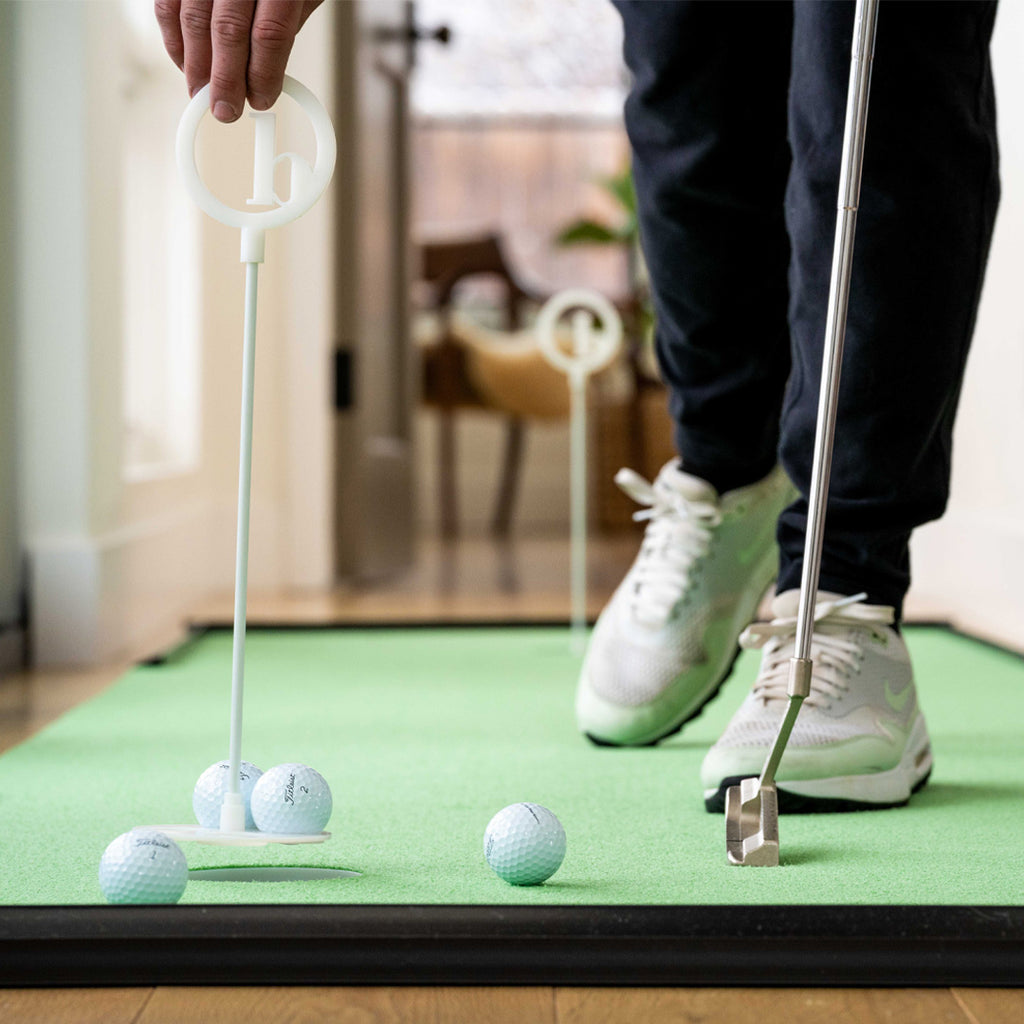 Wearing sneakers, someone practices putting golf balls on the BirdieBall Build Your Own RollTech™ Indoor Putting Mat (starting at $90), using a putter and aiming at small circular targets.